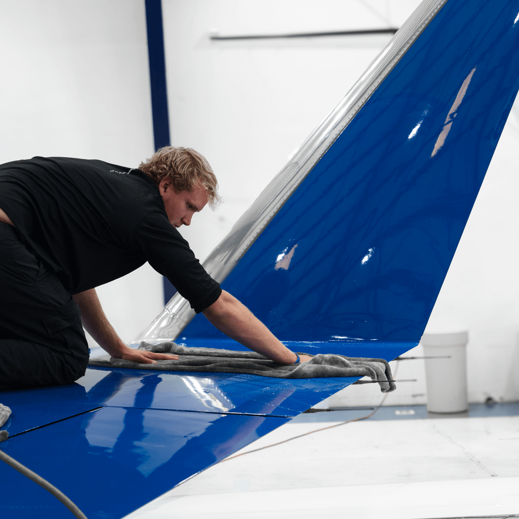 Detailer performing aircraft exterior detailing dry wash on blue airplane wing inside SDL, Scottsdale Airport hangar
